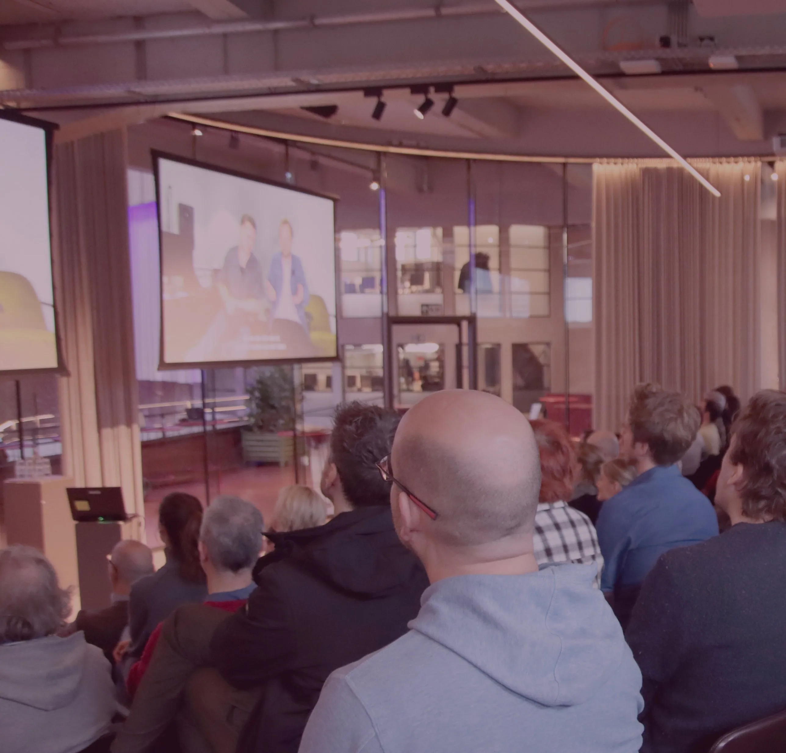 Publiek volgt een presentatie op grote schermen tijdens een evenement